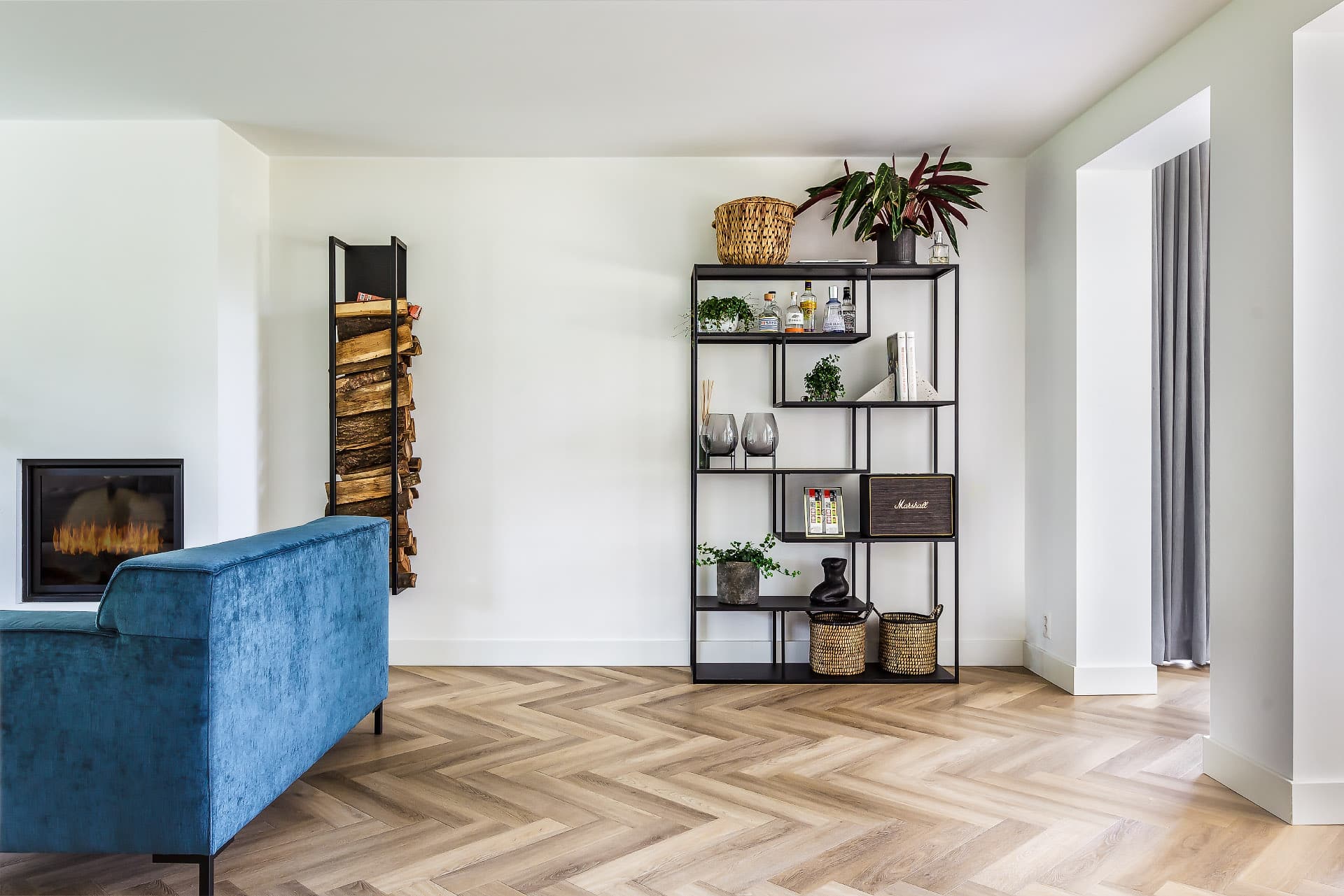 Een strak ingerichte open ruimte van een woonkamer met een eiken visgraat vloer en gashaard.